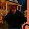 A person wearing a devil mask and a black cloak stands in front of a house decorated for Halloween, holding a skull. Produktbild-Vorschau