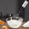 A hand mixer is shown in use, whipping egg whites in a glass bowl, with croissants and eggs in the foreground and kitchen appliances in the background. Podgląd zdjęcia produktu