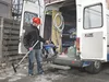 A man in a red hard hat is taking a vacuum cleaner out of the back of a white van. Produktbild-Vorschau