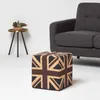 A cube-shaped ottoman with a Union Jack pattern sits in front of a dark gray sofa, next to a small side table with a potted plant. Náhled obrázku produktu