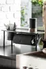 A black metal shelf with kitchen items, including a paper towel holder and cutlery holder, on a dark countertop. Náhled obrázku produktu