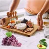 A person arranging a cheese board with various cheeses, fruits, nuts, and cheese knives. Náhľad obrázku produktu