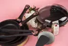A collection of cookware, including frying pans, tongs, a spatula, and a bag of grain, arranged on a pink surface. Náhľad obrázku produktu