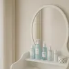 A vanity table with several cosmetic bottles on its shelf, reflected in a mirror. Voir les images du produit