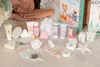 A collection of bath and body products arranged on a surface with a person resting their head on their hands in the background. Produktbild-Vorschau