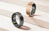 Two smart rings, one black and one rose gold, are displayed on a light-colored, tiered surface. Voir les images du produit