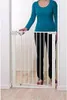 A person stands next to a white metal baby gate installed in a doorway. Produktbild-Vorschau