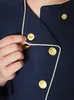 Close-up of a person's hand adjusting a gold button on a dark blue uniform with gold trim. Produktbild-Vorschau