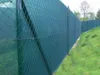 A green chain-link fence with a privacy screen attached, running along a grassy slope. Podgląd zdjęcia produktu