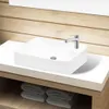 A white ceramic sink with a silver faucet is placed on a white countertop, with a wooden wall in the background and folded towels on a shelf below. Náhľad obrázku produktu