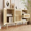 A light wood sideboard with cane detailing, featuring open doors and a drawer, styled with books, candles, and a decorative bird. Náhled obrázku produktu