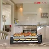 A raclette grill with food is placed on a wooden table in a kitchen. Náhľad obrázku produktu