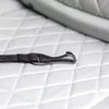 A close-up of a dog seatbelt strap and buckle on a white quilted surface. Produktbild-Vorschau
