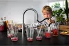 A young boy is using a kitchen faucet to fill glasses with red liquid. Produktbild-Vorschau