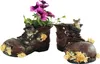 Two weathered brown boots are used as planters, with purple flowers and green foliage growing out of one, and small mouse figurines peeking out of both. Produktbild-Vorschau