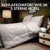 A luxurious bed with a duvet and pillows, set in a dimly lit, elegant bedroom. Produktbild-Vorschau