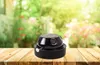 A black heater sits on a wooden table with a blurred garden in the background. Produktbild-Vorschau
