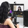 A person wearing headphones is shown in front of a computer screen, with a microphone and webcam set up for recording or streaming. Anteprima dell’immagine prodotto