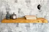 A wooden shelf mounted on a textured wall with decorative items. Produktbild-Vorschau