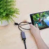 A person is holding a tablet that is displaying a video game. Cables are connected to the tablet and to an adapter. A potted plant is in the background. Voir les images du produit
