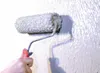 A hand is using a paint roller to apply a thick, gray substance to a textured wall. Anteprima dell’immagine prodotto