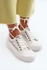 A pair of white lace-up sneakers with white laces tied around the ankles, worn by a person wearing light yellow cropped pants. Voir les images du produit