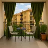 A balcony with two chairs, a small table, and plants, overlooking apartment buildings. Produktbild-Vorschau