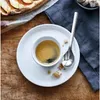 A close-up shot of an espresso cup and spoon on a saucer, with a slice of pie and a napkin in the background. Podgląd zdjęcia produktu