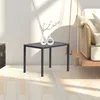 A small, dark gray square table with two white vases on top, placed on a light-colored wooden floor. Sunlight casts shadows on the wall behind it, and a part of a hanging swing chair is visible on the right. Produktbild-Vorschau