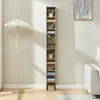 A tall, narrow bookshelf filled with items stands against a light gray wall, next to a floor lamp. Náhľad obrázku produktu