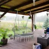 A macrame hanging chair on a wooden deck with a garden view. Náhľad obrázku produktu