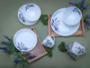 A flat lay of a 16-piece porcelain dinnerware set with a lavender motif, arranged with decorative moss and lavender sprigs on a green background. Náhľad obrázku produktu