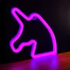 A neon unicorn sign is displayed against a dark background, with a wooden surface in the foreground. Voir les images du produit