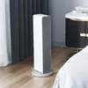 A white tower fan heater is placed on a wooden floor next to a bed and a nightstand. Voir les images du produit