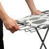 A close-up view of a person's hands adjusting a part of an ironing board. Podgląd zdjęcia produktu