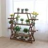 A wooden plant stand with multiple shelves filled with various potted plants, placed indoors near a window with sheer curtains. Anteprima dell’immagine prodotto
