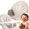 A baby covered in chocolate sits in a high chair, with a separate image of the high chair seat in the background. Produktbild-Vorschau