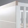 Close-up view of the corner of a crib or bed frame, showing the join between a white panel and a wooden trim. Produktbild-Vorschau