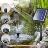 A solar-powered water pump fountain is shown operating in a pond, with a solar panel mounted on a pole nearby. Inset circles show different nozzle attachments and water spray patterns. Podgląd zdjęcia produktu