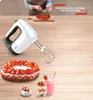 A white and gray Tefal hand mixer is placed on a wooden table next to a strawberry tart, a small pastry, and two glasses of strawberry smoothie. Produktbild-Vorschau