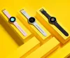 Three smartwatches in different colors are displayed on yellow geometric stands against a yellow background. Podgląd zdjęcia produktu