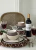A table setting with dinnerware, a bottle of wine, and pinecones. Produktbild-Vorschau