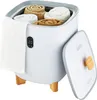A white towel warmer bucket with rolled towels inside, sitting on wooden legs. The lid is open, revealing a wooden handle. A white towel hangs from the side. Náhled obrázku produktu