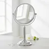 A silver vanity mirror is placed on a countertop next to a white orchid. Podgląd zdjęcia produktu