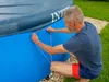 A man is securing a cover onto an oval pool. Produktbild-Vorschau