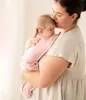 A woman is holding a baby wrapped in a pink swaddle. Anteprima dell’immagine prodotto