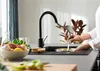 A person is using a black kitchen faucet to wash dishes in a sink. Produktbild-Vorschau