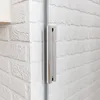 A close-up view of a shower door handle against a white brick-like wall. Produktbild-Vorschau