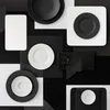 A flat lay arrangement of various plates and saucers in black and white, with textured surfaces. Produktbild-Vorschau