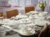 A formal dining table setting with white tableware, glassware, and a floral arrangement. Produktbild-Vorschau